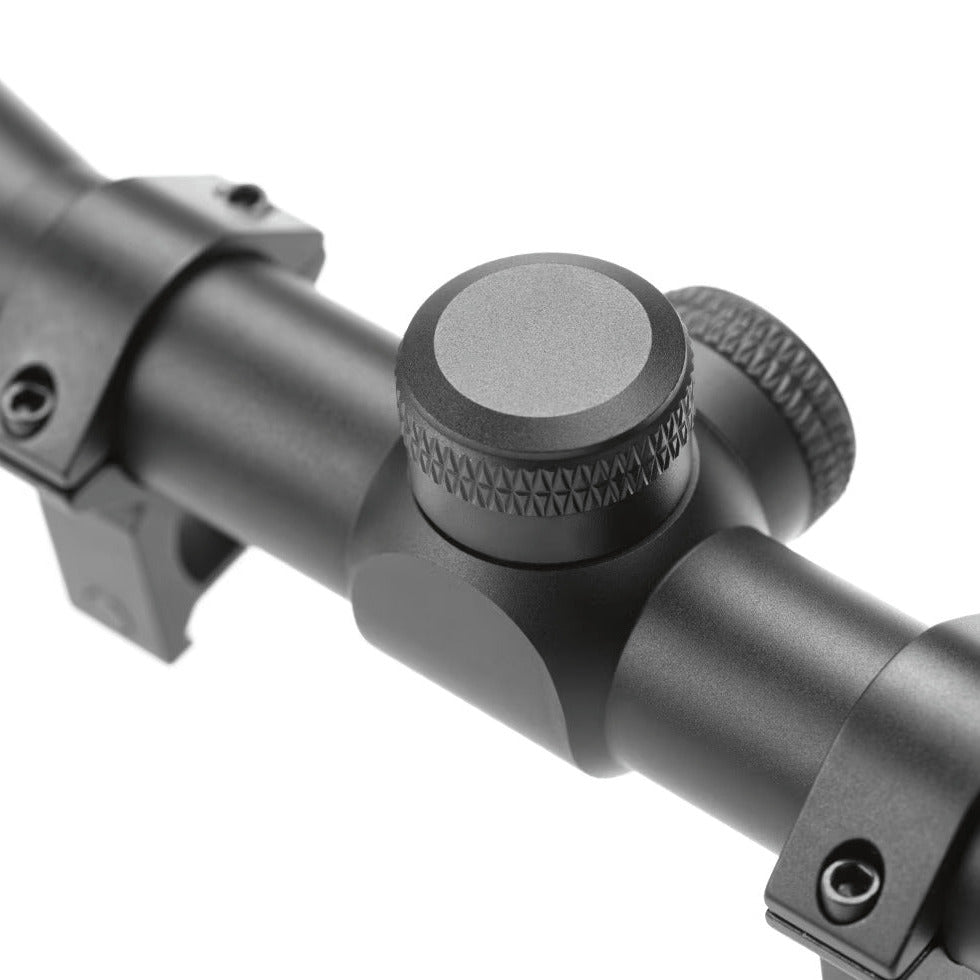 Close-up of a black rifle scope with adjustment knobs and mounting rings on a white background.